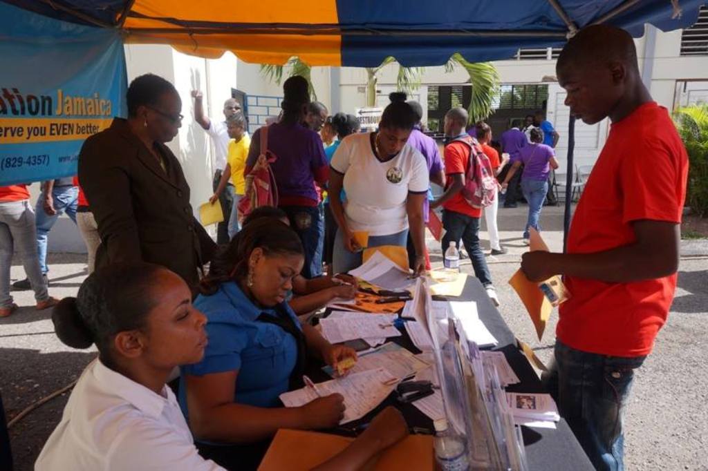 A team from the Tax Administration of Jamaica process documents at the event, while a youngster (standing right) observes the process taking place. Assisting with the documents is CDA’s St. Ann Office Attendant, Ishahana Christie (standing centre). 