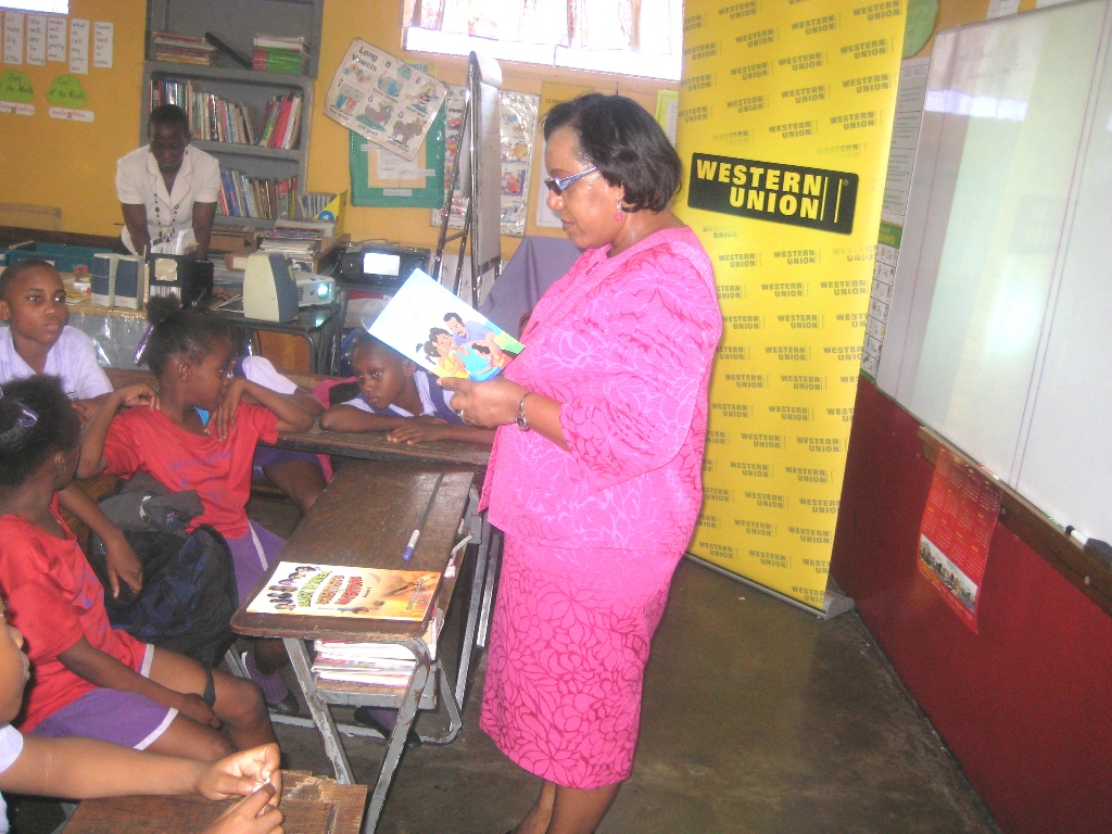 Chief Executive Officer of the Child Development Agency (CDA), Rosalee Gage-Grey, reads a portion of the CDA’s ‘Act Right, Treat me Right!’  child abuse prevention book, to a group of students at the recent launch of the Western Union’s I promise to Lend Encouragement to Develop Growth in Education (I PLEDGE) Programme, and Reading Week, held at Ascot Primary School, in Portmore, St. Catherine.